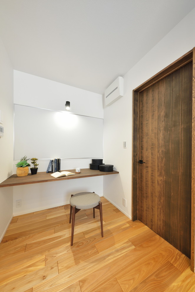 Réalisation d'un petit bureau minimaliste avec un mur blanc, un sol en bois brun, un bureau intégré et un sol marron.