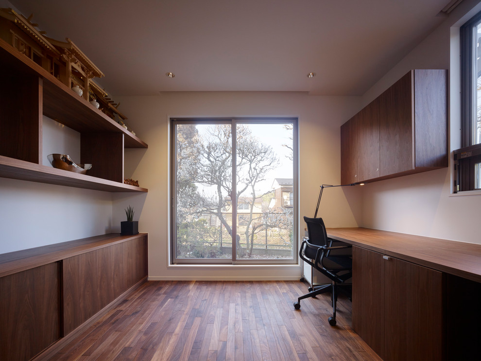 Diseño de despacho moderno con paredes blancas, suelo de madera oscura, escritorio empotrado y suelo marrón