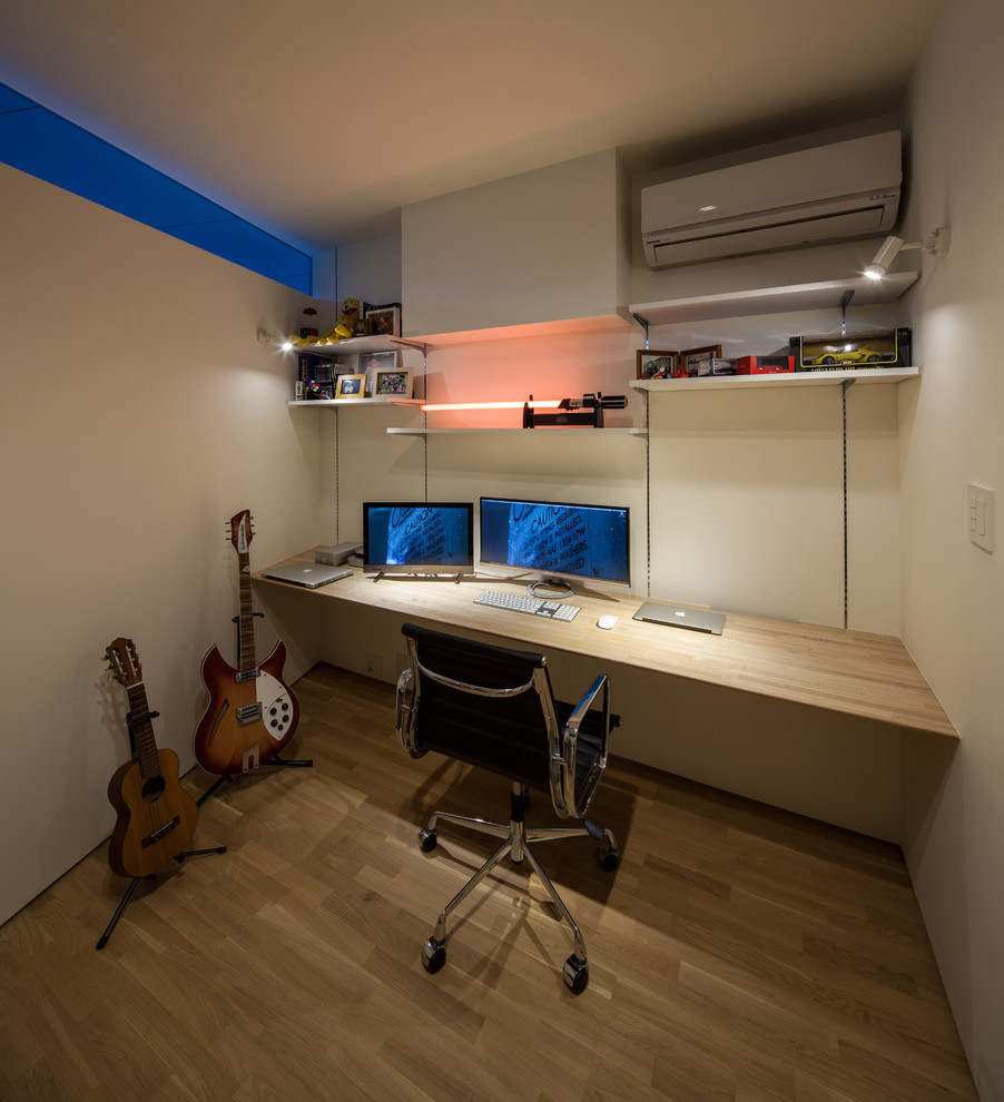 Cette photo montre un petit bureau tendance avec un mur blanc, un sol en bois brun, un bureau intégré et un sol marron.