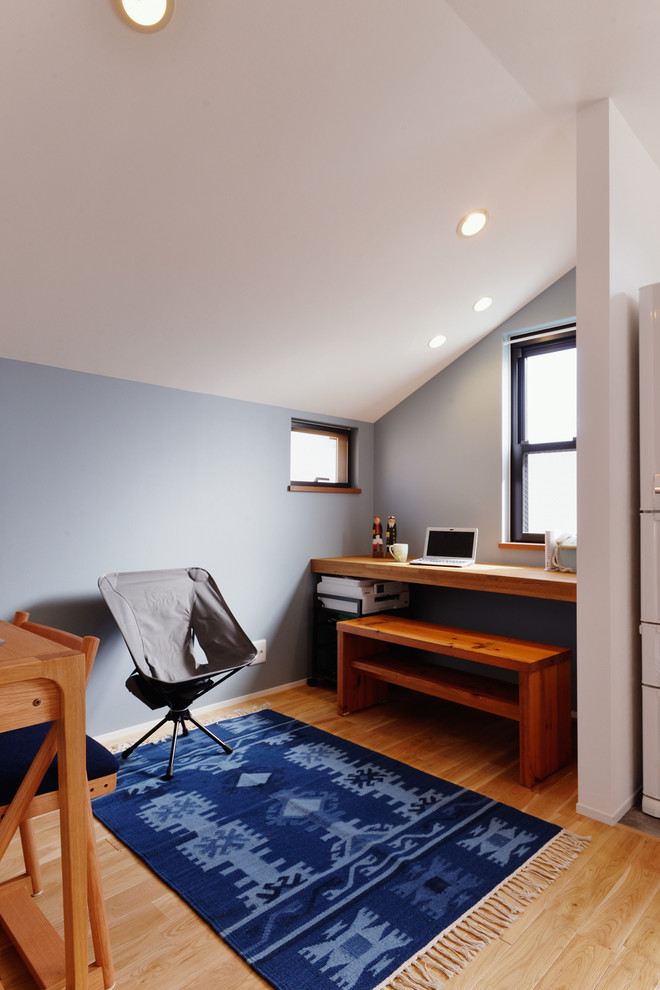 Inredning av ett modernt litet arbetsrum, med blå väggar, mellanmörkt trägolv, ett inbyggt skrivbord och brunt golv
