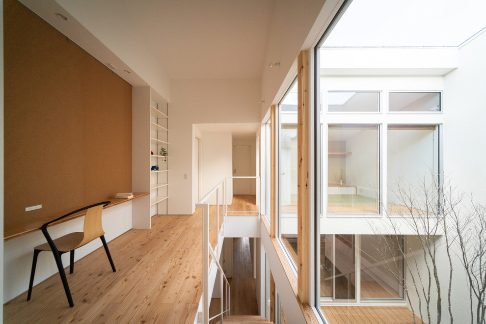 Exempel på ett minimalistiskt arbetsrum, med ett bibliotek, vita väggar, ljust trägolv, ett inbyggt skrivbord och brunt golv