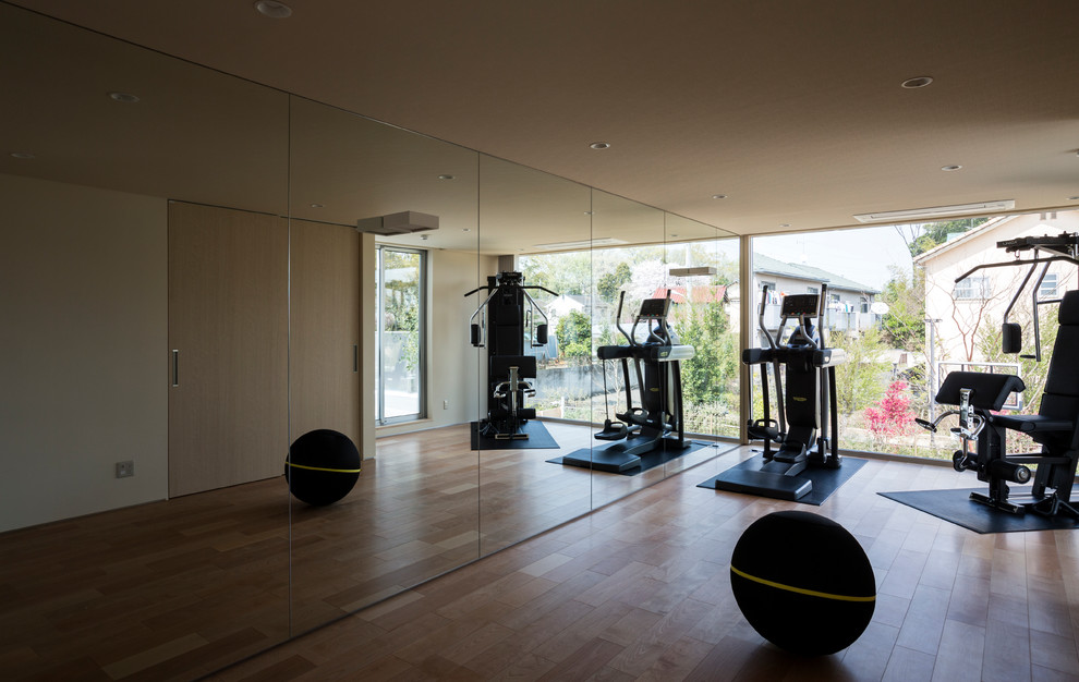 Modelo de sala de pesas minimalista grande con paredes beige y suelo de madera en tonos medios