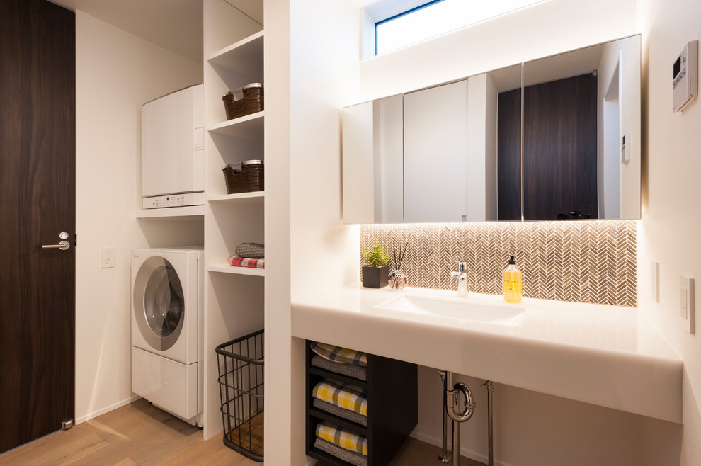 Modelo de lavadero minimalista con armarios abiertos, paredes blancas, suelo de madera pintada, lavadora y secadora apiladas, suelo marrón, encimeras blancas y fregadero bajoencimera