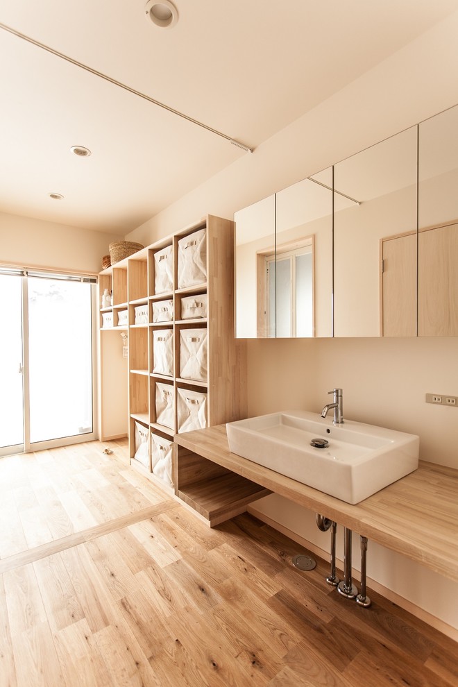 Cette photo montre une petite buanderie linéaire moderne en bois clair dédiée avec un placard sans porte, un plan de travail en bois, un mur blanc et un sol en bois brun.