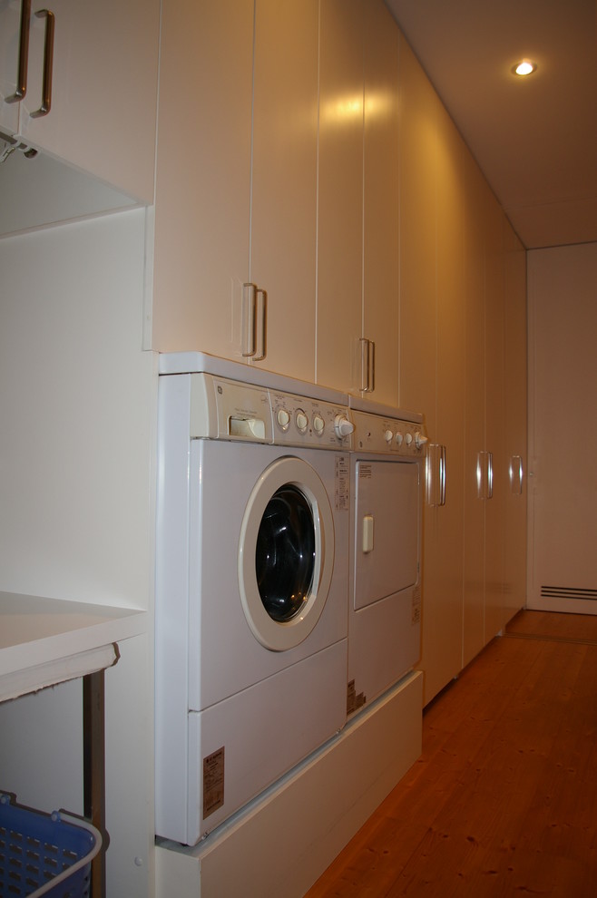 Immagine di un ripostiglio-lavanderia minimalista di medie dimensioni con ante lisce, ante bianche, pareti bianche, pavimento in legno massello medio e lavatrice e asciugatrice affiancate