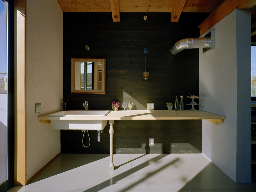 Aménagement d'une buanderie linéaire industrielle avec un évier posé, un plan de travail en bois, un mur noir, un placard sans porte, un sol gris et un plan de travail beige.