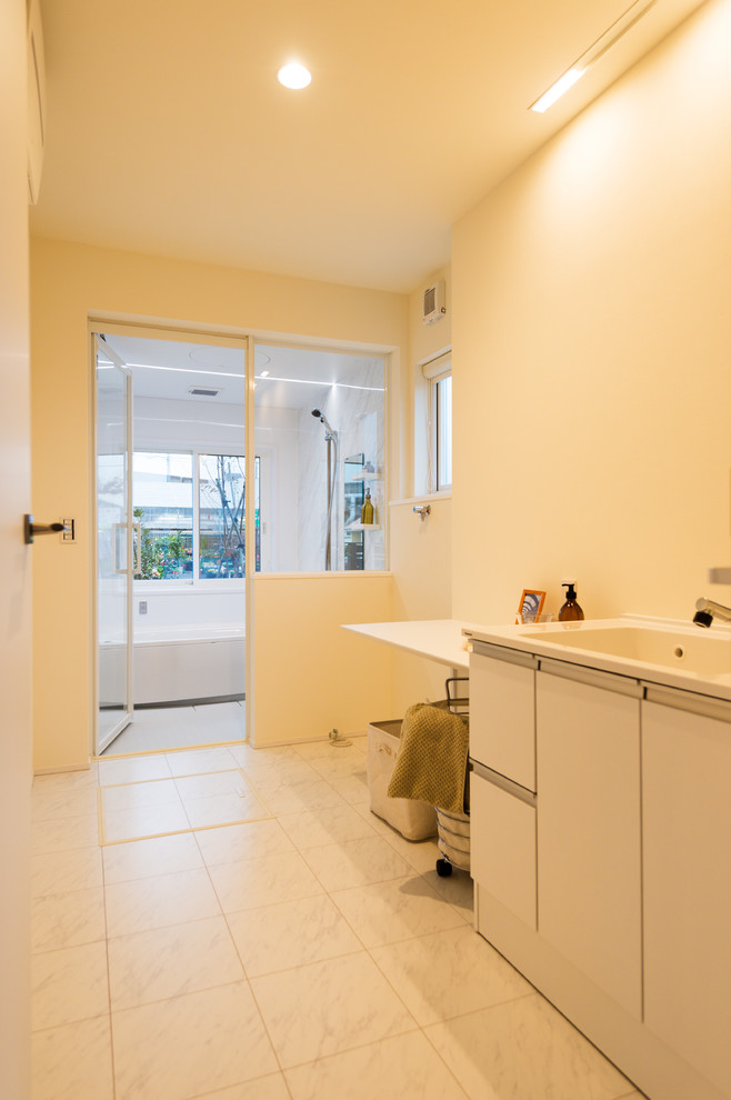 Example of an asian beige floor laundry room design in Other with an integrated sink, flat-panel cabinets, white cabinets, beige walls and beige countertops
