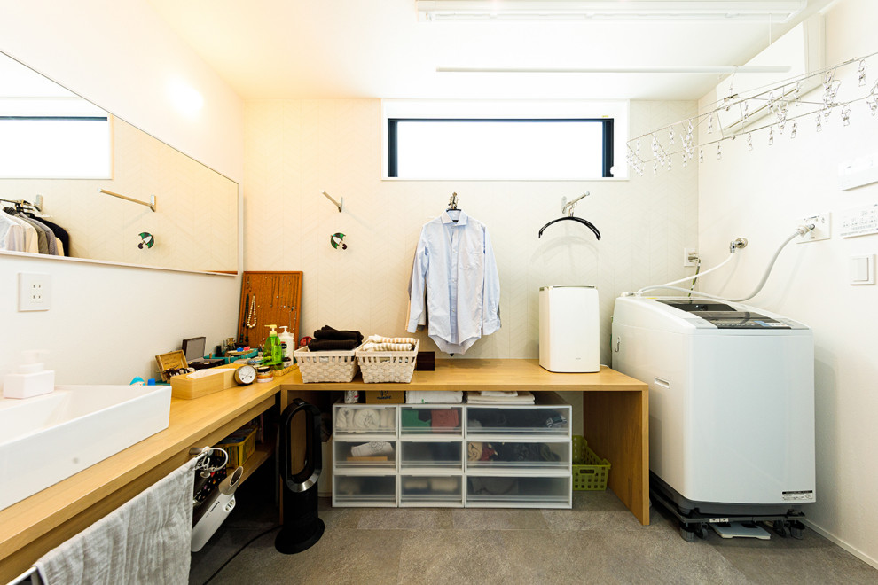 東京都下にあるお手頃価格の中くらいなインダストリアルスタイルのおしゃれな家事室 (L型、白い壁、グレーの床、ベージュのキッチンカウンター、ドロップインシンク、オープンシェルフ、茶色いキャビネット、木材カウンター、セラミックタイルの床、洗濯乾燥機) の写真