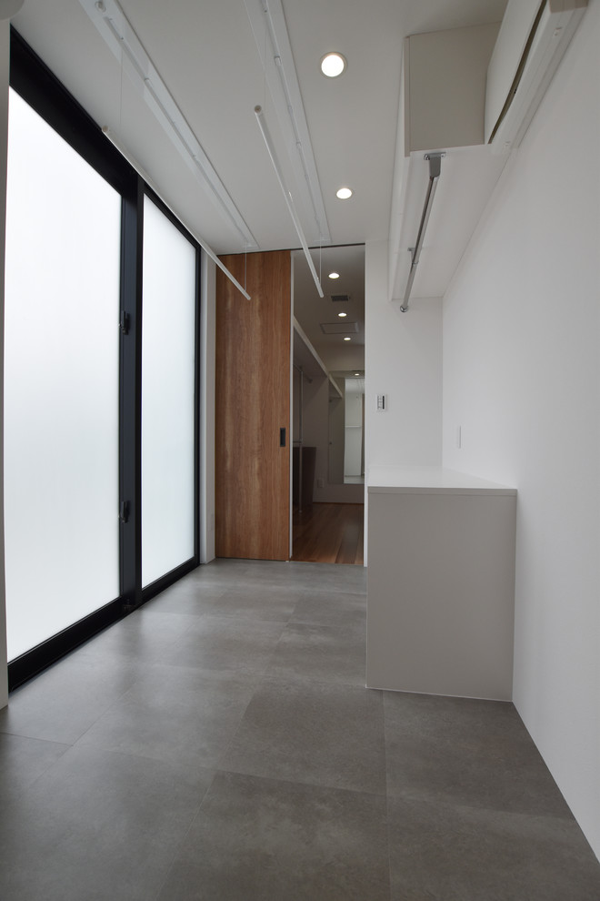 Réalisation d'une buanderie minimaliste multi-usage avec des portes de placard blanches, un mur blanc, un sol en vinyl, un lave-linge séchant, un sol gris et un plan de travail blanc.