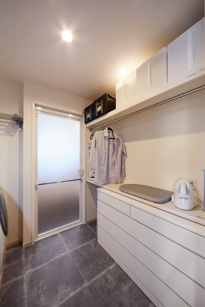 Modelo de lavadero escandinavo con puertas de armario blancas, paredes blancas, suelo de cemento, suelo gris y encimeras blancas