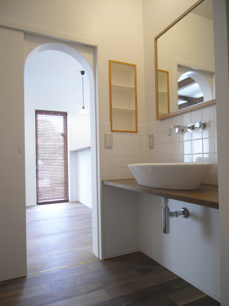 Foto på en mellanstor funkis bruna tvättstuga, med träbänkskiva, vita väggar, mörkt trägolv, en nedsänkt diskho, öppna hyllor och brunt golv