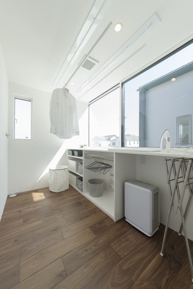 Ejemplo de cuarto de lavado minimalista con paredes blancas, suelo de madera oscura, suelo marrón y encimeras blancas