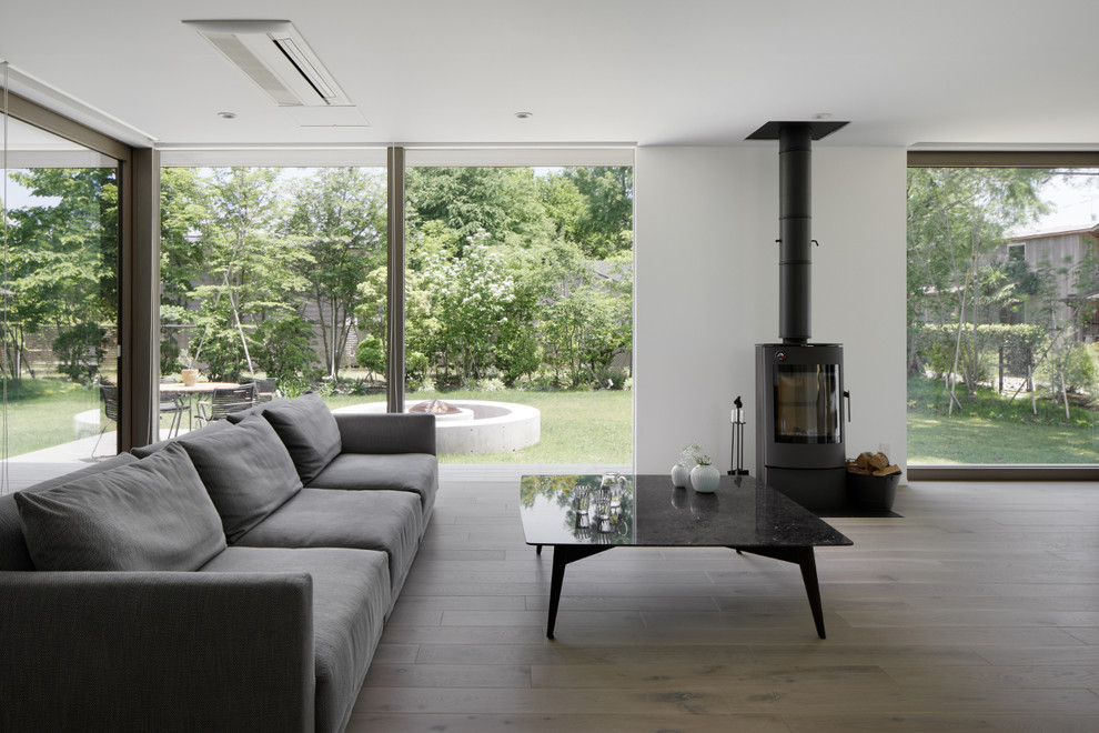 Ejemplo de salón abierto minimalista con paredes blancas, suelo de madera clara, estufa de leña, suelo gris y marco de chimenea de metal