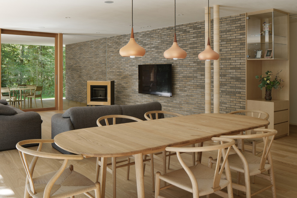 Foto på ett minimalistiskt allrum med öppen planlösning, med beige väggar, ljust trägolv, en spiselkrans i tegelsten och en väggmonterad TV