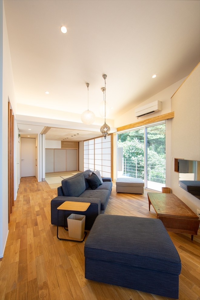 Großes, Offenes Asiatisches Wohnzimmer mit weißer Wandfarbe, TV-Wand, braunem Holzboden und braunem Boden in Sonstige