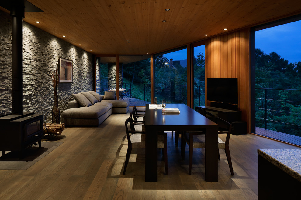 Diseño de salón abierto moderno con paredes grises, suelo de madera oscura, estufa de leña, marco de chimenea de baldosas y/o azulejos y televisor independiente