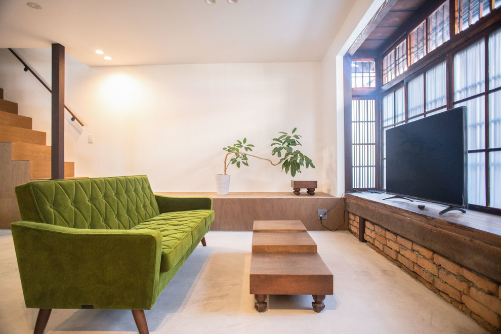 Cette image montre un salon asiatique ouvert avec un mur blanc, sol en béton ciré, un téléviseur indépendant et un sol gris.