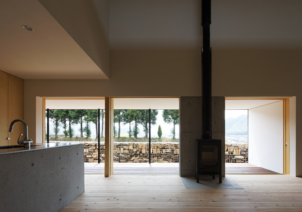 Ejemplo de salón abierto moderno grande con paredes blancas, suelo de madera clara, estufa de leña, marco de chimenea de hormigón y suelo gris