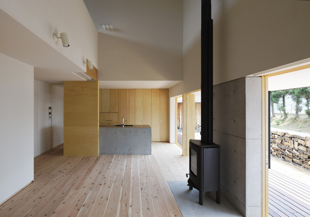 Modelo de salón abierto minimalista grande con paredes blancas, suelo de madera clara, estufa de leña, marco de chimenea de hormigón y suelo gris