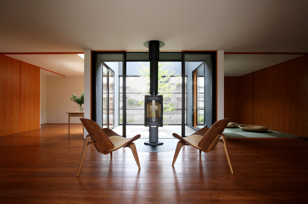 Imagen de salón abierto de estilo zen pequeño con paredes blancas, suelo de madera en tonos medios, estufa de leña, televisor retractable y suelo marrón