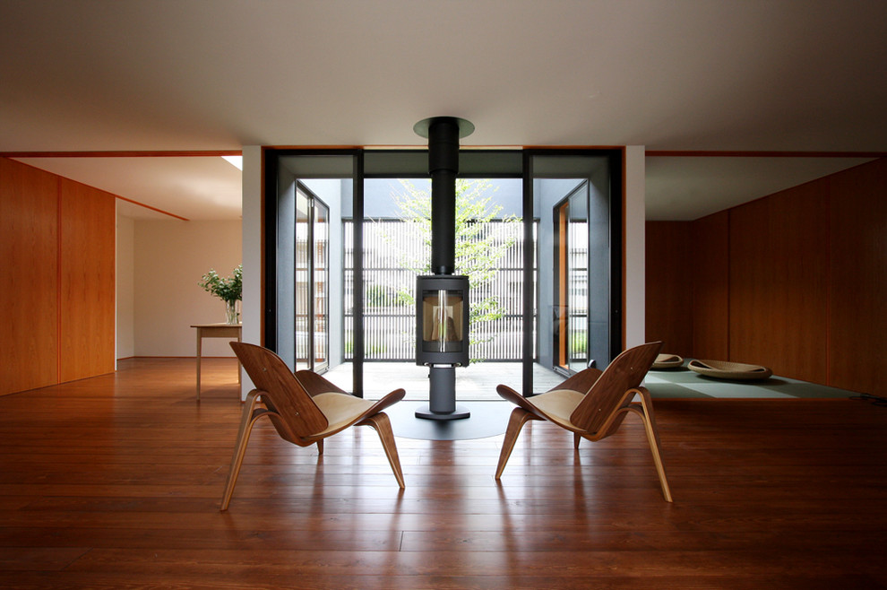 Photo of a small world-inspired open plan living room in Other with white walls, medium hardwood flooring, a wood burning stove, a concealed tv and brown floors.