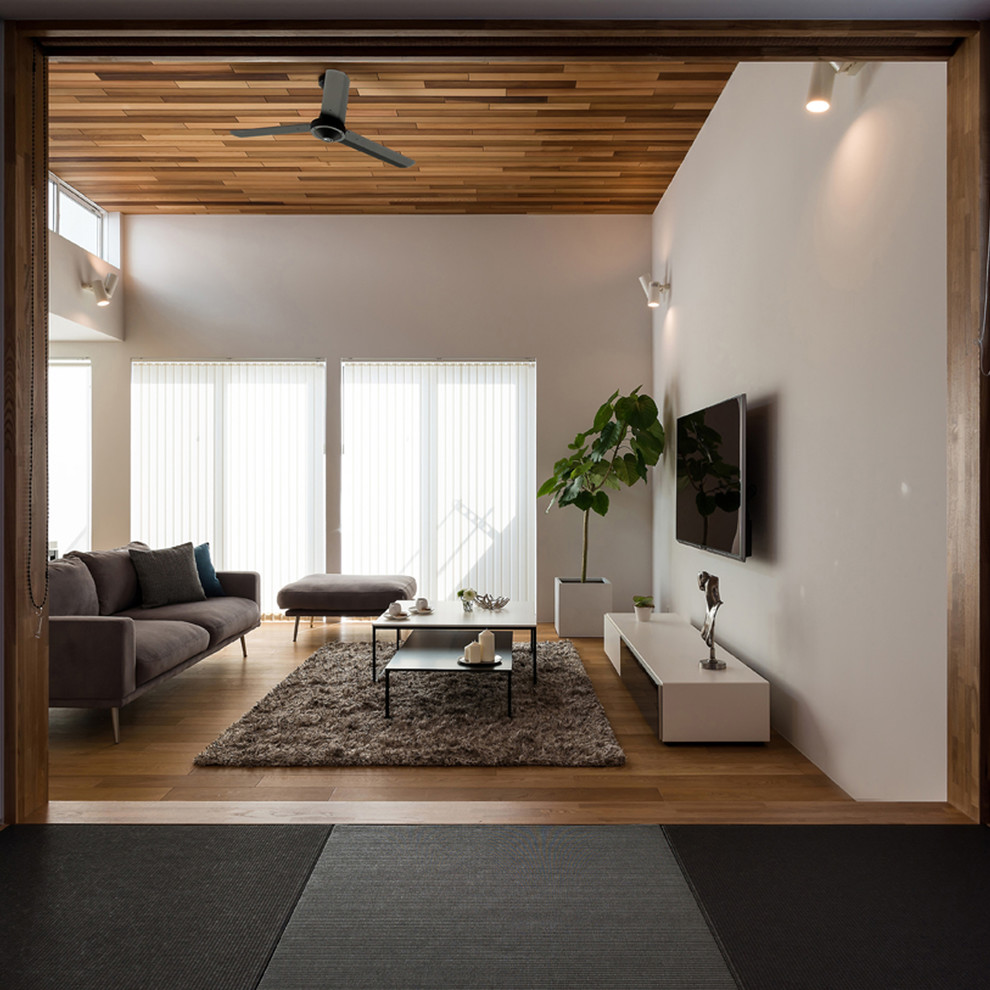 Inredning av ett modernt vardagsrum, med vita väggar, mellanmörkt trägolv, en väggmonterad TV och brunt golv