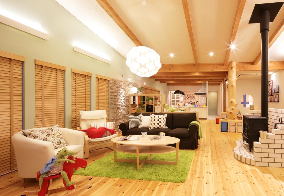 Ejemplo de salón abierto nórdico con paredes verdes, suelo de madera clara, estufa de leña y marco de chimenea de ladrillo