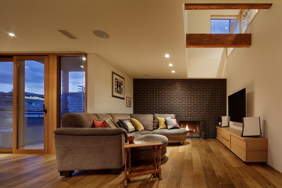 Large world-inspired open plan living room in Tokyo with white walls, medium hardwood flooring, a standard fireplace, a tiled fireplace surround, a wall mounted tv and brown floors.