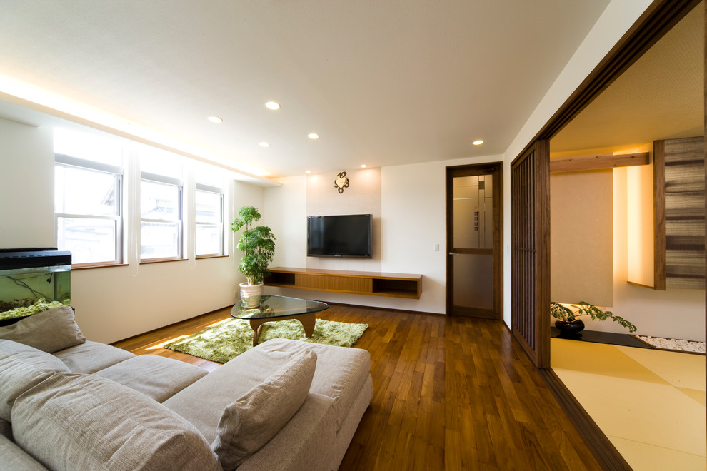 Inredning av ett asiatiskt vardagsrum, med vita väggar, mellanmörkt trägolv och en väggmonterad TV