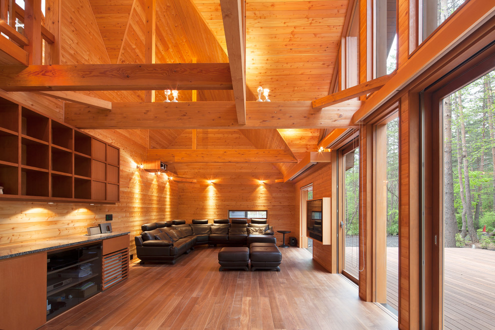 Diseño de salón abierto de estilo zen con paredes marrones, suelo de madera en tonos medios, televisor colgado en la pared y suelo marrón