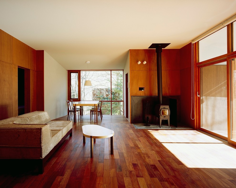 Exempel på ett litet modernt allrum med öppen planlösning, med bruna väggar, mörkt trägolv, en öppen vedspis, en spiselkrans i betong och brunt golv