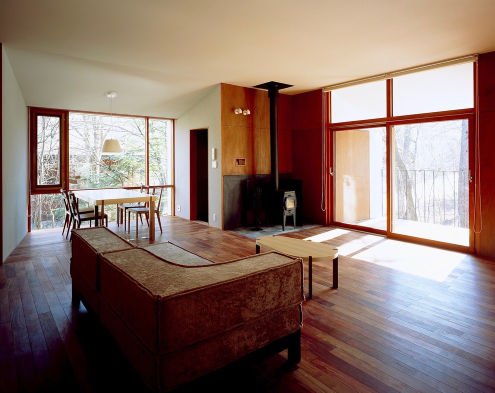 Foto de salón abierto moderno pequeño sin televisor con paredes marrones, suelo de madera oscura, estufa de leña, marco de chimenea de hormigón y suelo marrón