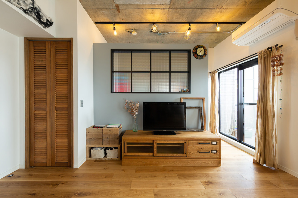 На фото: открытая гостиная комната в стиле лофт с белыми стенами, отдельно стоящим телевизором и коричневым полом с