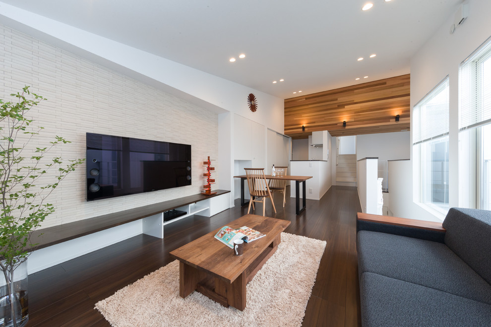 Свежая идея для дизайна: гостиная комната в современном стиле с белыми стенами, темным паркетным полом, телевизором на стене и коричневым полом - отличное фото интерьера