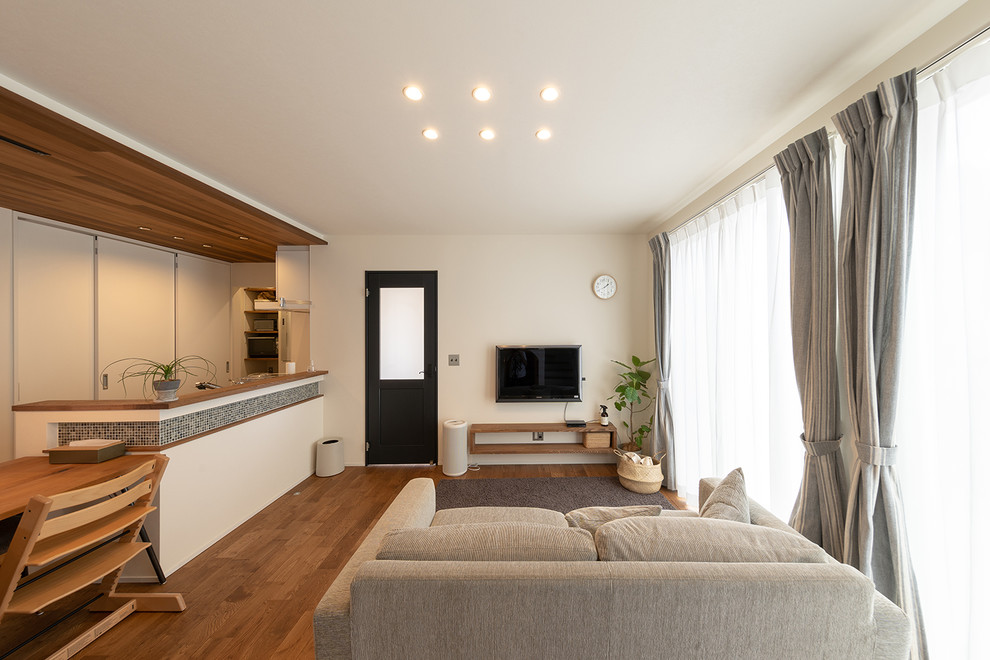 Ejemplo de salón abierto de estilo zen sin chimenea con paredes blancas, suelo de madera en tonos medios, televisor colgado en la pared y suelo marrón