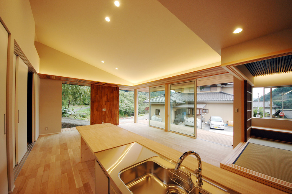 Mittelgroßes, Offenes Asiatisches Wohnzimmer mit weißer Wandfarbe, hellem Holzboden und TV-Wand in Sonstige