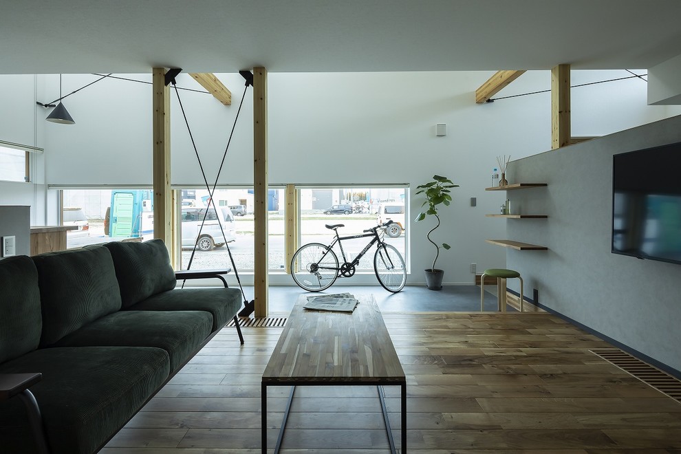 Idee per un soggiorno industriale aperto con pareti grigie, pavimento in legno massello medio, TV a parete e pavimento marrone