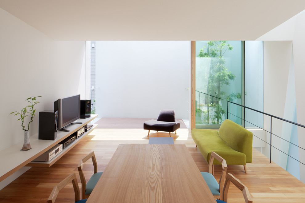 Imagen de salón actual sin chimenea con paredes blancas, suelo de madera clara y televisor independiente