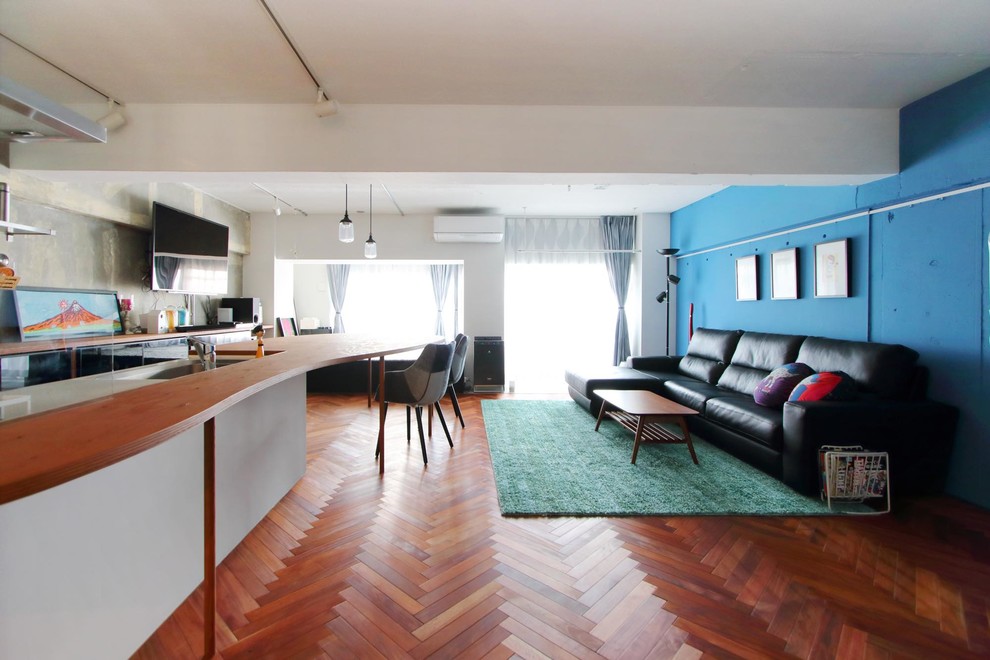 Modelo de salón abierto asiático con paredes azules, suelo de madera oscura, televisor colgado en la pared y suelo marrón