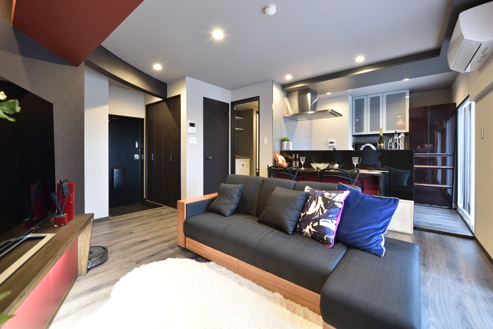 Offenes Modernes Wohnzimmer mit schwarzer Wandfarbe, gebeiztem Holzboden, freistehendem TV und grauem Boden in Sonstige