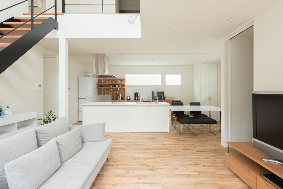 Exempel på ett modernt allrum med öppen planlösning, med vita väggar, ljust trägolv, en fristående TV och brunt golv