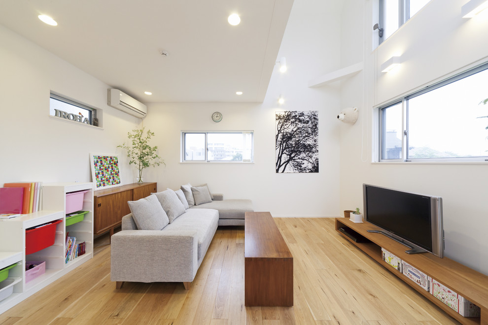 Exempel på ett modernt allrum med öppen planlösning, med vita väggar, ljust trägolv, en fristående TV och beiget golv