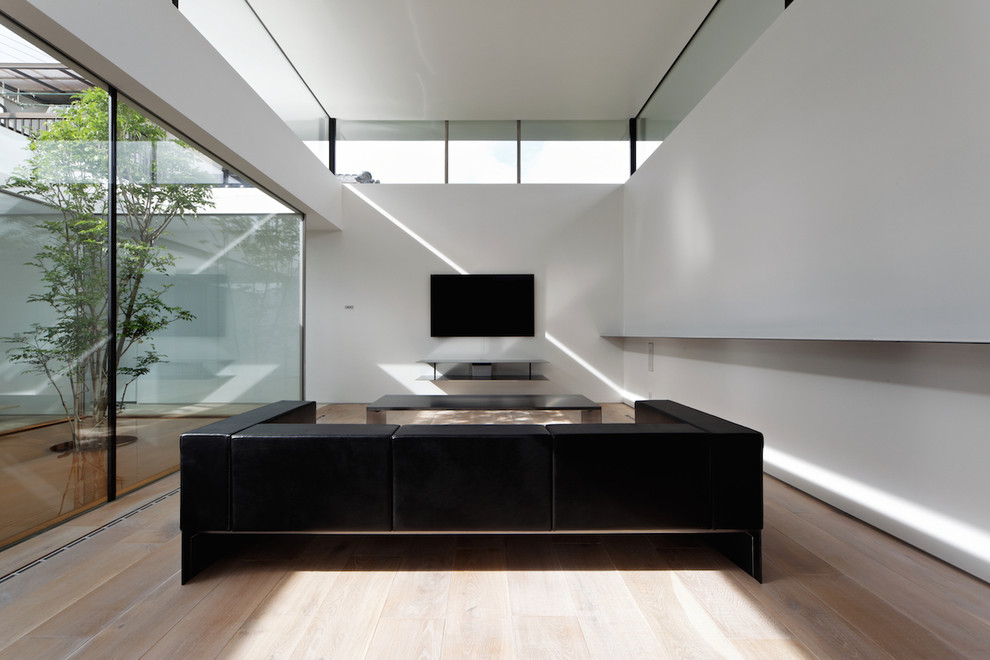 Modern inredning av ett stort allrum med öppen planlösning, med vita väggar, ljust trägolv och en väggmonterad TV
