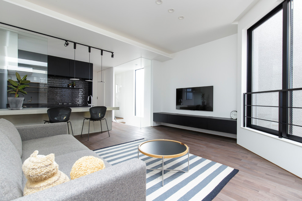 Modernes Wohnzimmer mit weißer Wandfarbe, gebeiztem Holzboden, TV-Wand und grauem Boden in Sonstige