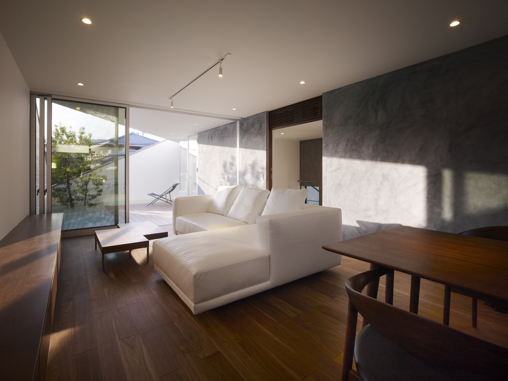 Modelo de salón abierto y blanco minimalista de tamaño medio con paredes grises, suelo de contrachapado, televisor colgado en la pared y suelo marrón