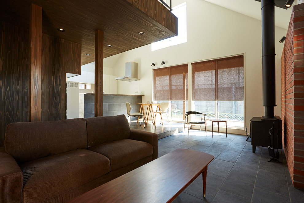 Exempel på ett litet modernt allrum med öppen planlösning, med ett finrum, orange väggar, klinkergolv i porslin, en spiselkrans i tegelsten, en fristående TV, svart golv och en öppen vedspis
