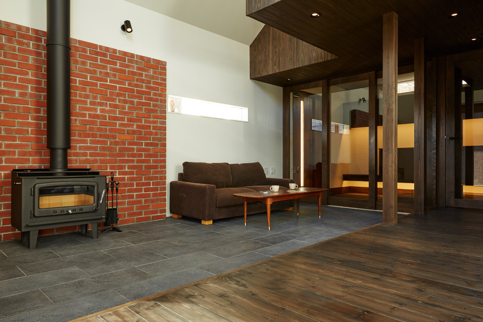 Idées déco pour un petit salon rétro ouvert avec un poêle à bois, un manteau de cheminée en brique, un mur orange, un sol en carrelage de porcelaine, un téléviseur indépendant et un sol noir.