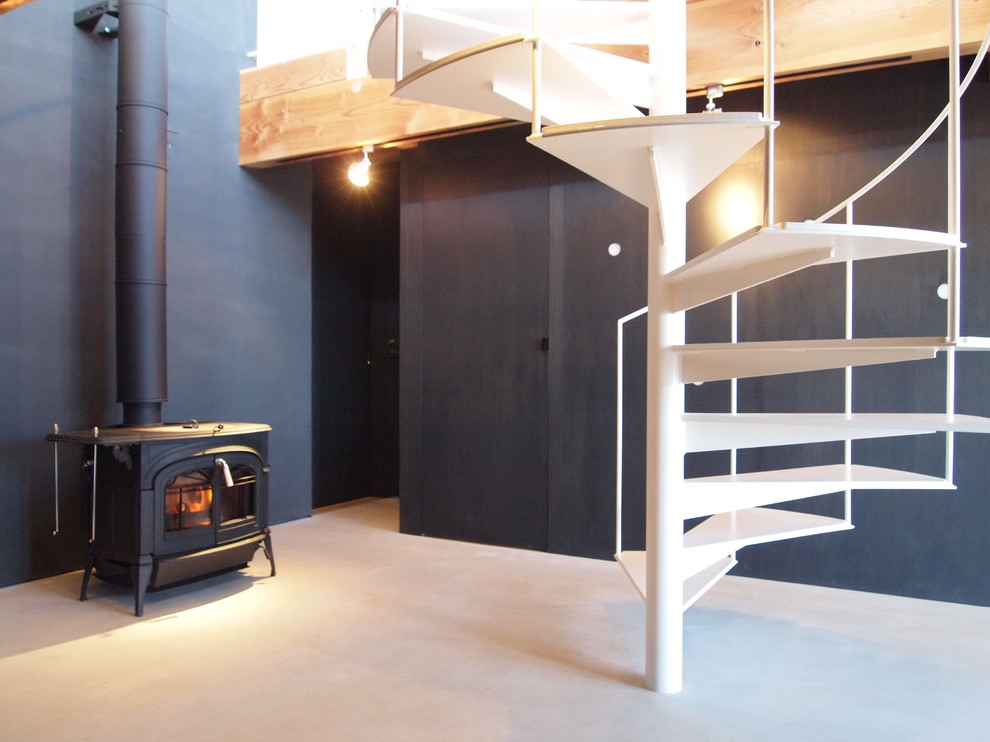 Cette image montre un salon minimaliste avec un mur noir, sol en béton ciré, un poêle à bois et un manteau de cheminée en plâtre.