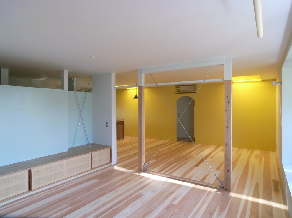 Ejemplo de salón abierto asiático grande con paredes amarillas, suelo de madera clara y televisor independiente