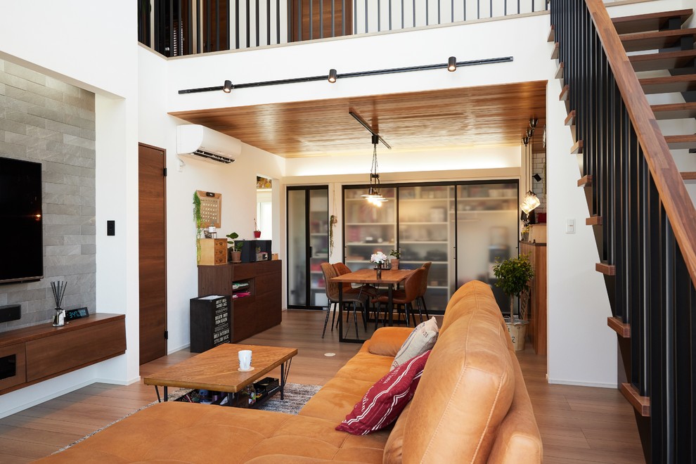 Foto di un soggiorno moderno aperto con pareti bianche, pavimento in legno massello medio, TV a parete e pavimento marrone